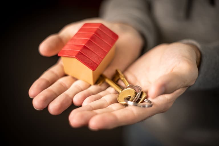 Pessoa segurando miniatura de casa e chaves para representar contrato de aluguel