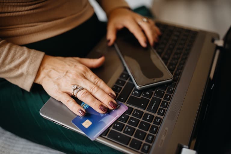 Pessoa segurando cartão de crédito sobre notebook e smartphone